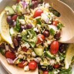 Close up of a lemon orzo salad tossed with feta, herbs, and veggies.