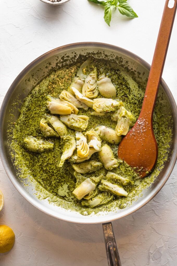 Artichokes being stirred into a light pesto cream sauce.