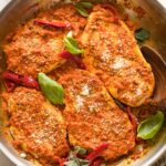 Skillet full of roasted red pepper chicken garnished with herbs and Parmesan.