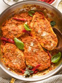 Skillet full of roasted red pepper chicken garnished with herbs and Parmesan.