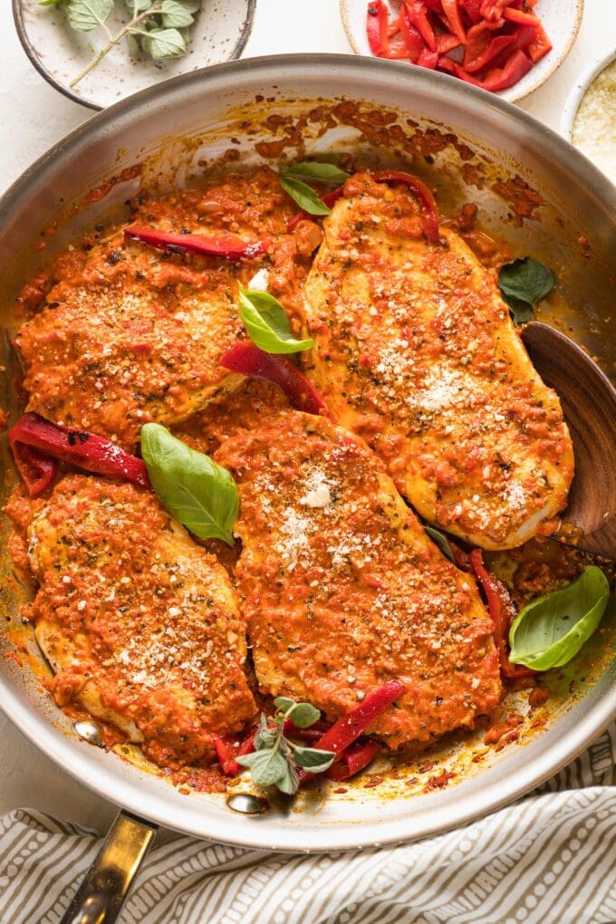 Skillet full of roasted red pepper chicken garnished with herbs and Parmesan.
