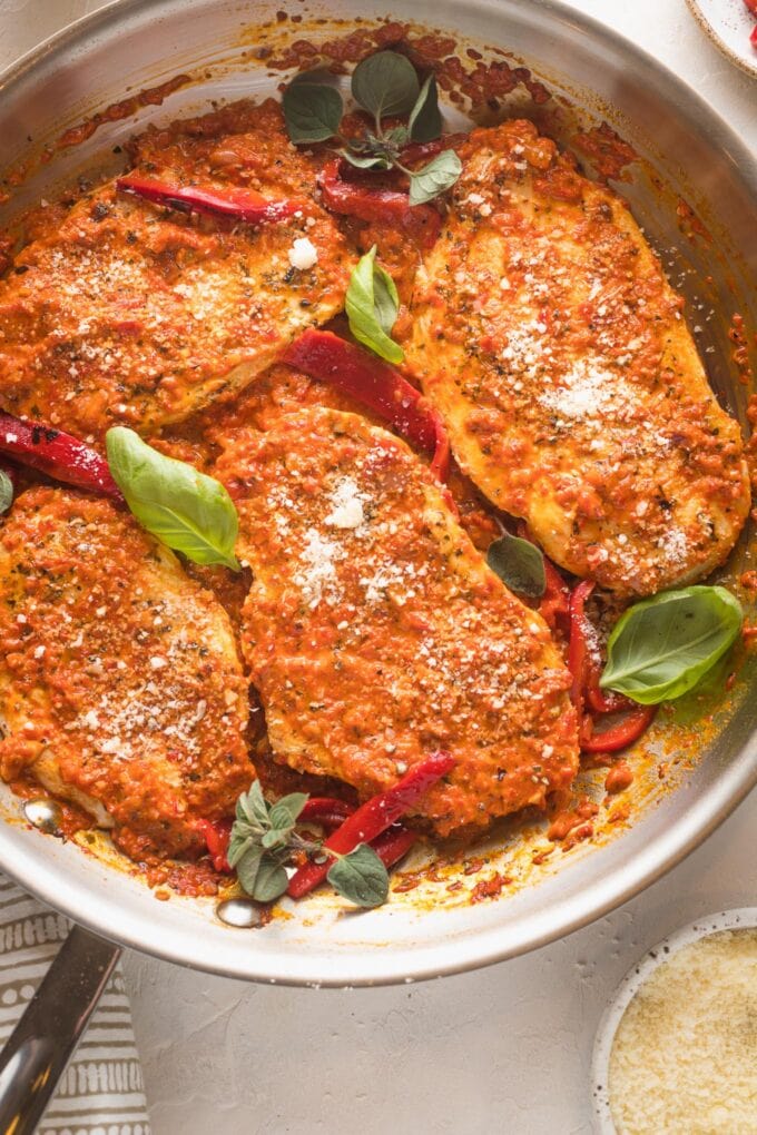 Skillet full of roasted red pepper chicken garnished with herbs and Parmesan.