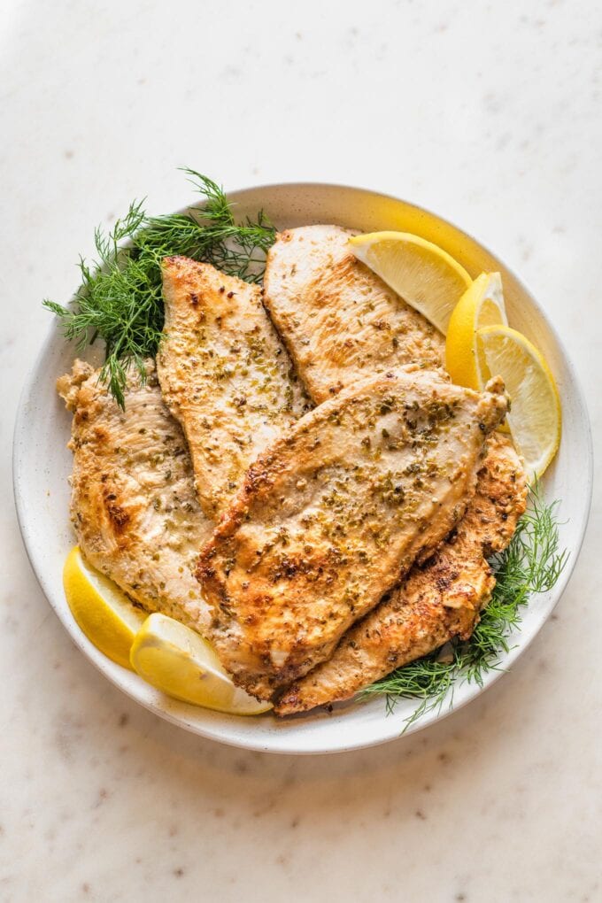 White plate holding a pile of Greek marinated chicken breasts.