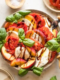 Earth-toned plate filled with a peach Caprese salad drizzled with balsamic glaze and fresh basil leaves.