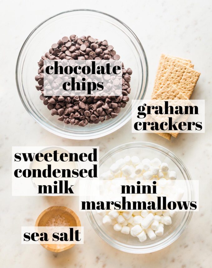 Prep bowls holding chocolate chips, graham crackers, mini marshmallows, and sea salt, along with a can of sweetened condensed milk.