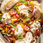 Platter with marinated tomatoes, burrata, pine nuts, and bread for serving.