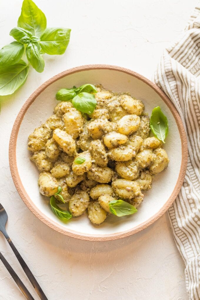 Small wooden bowl with a serving of creamy pesto gnocchi.