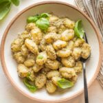 Small wooden bowl with a serving of creamy pesto gnocchi.