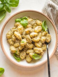 Small wooden bowl with a serving of creamy pesto gnocchi.