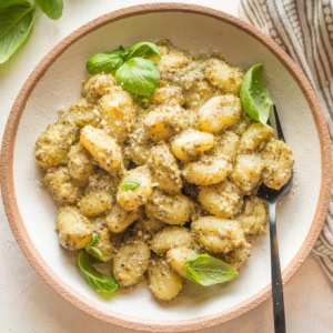 Small wooden bowl with a serving of creamy pesto gnocchi.