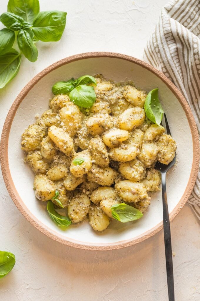 Small wooden bowl with a serving of creamy pesto gnocchi.