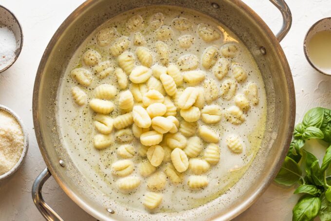 Large skillet with gnocchi piled high in the middle of a light pesto cream sauce.