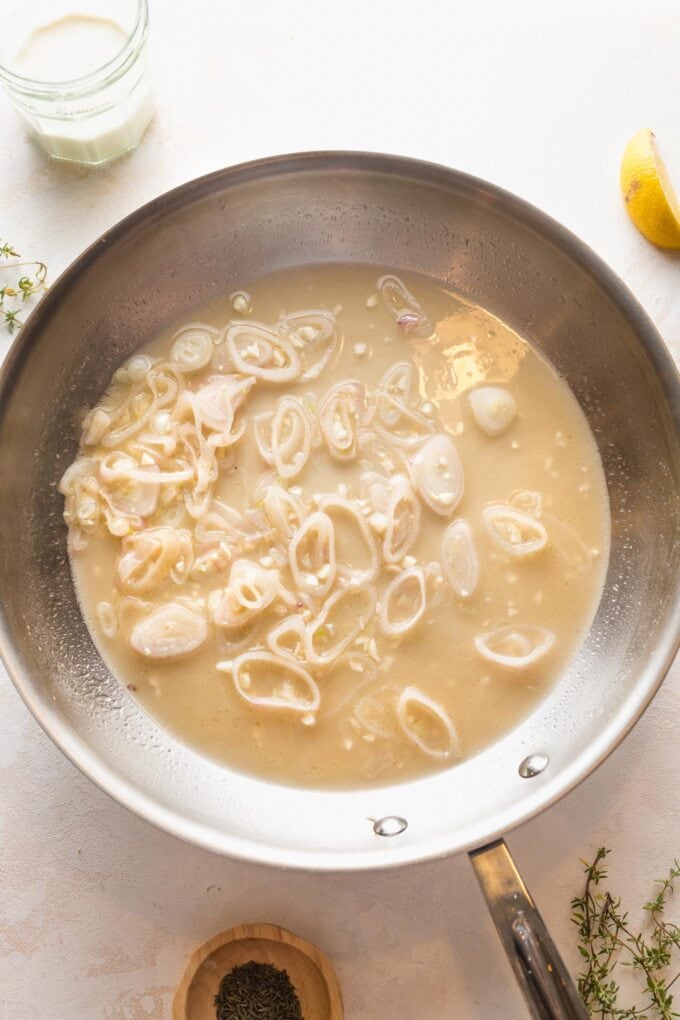 Large skillet with cooked shallots, garlic, and a simmering white wine sauce.