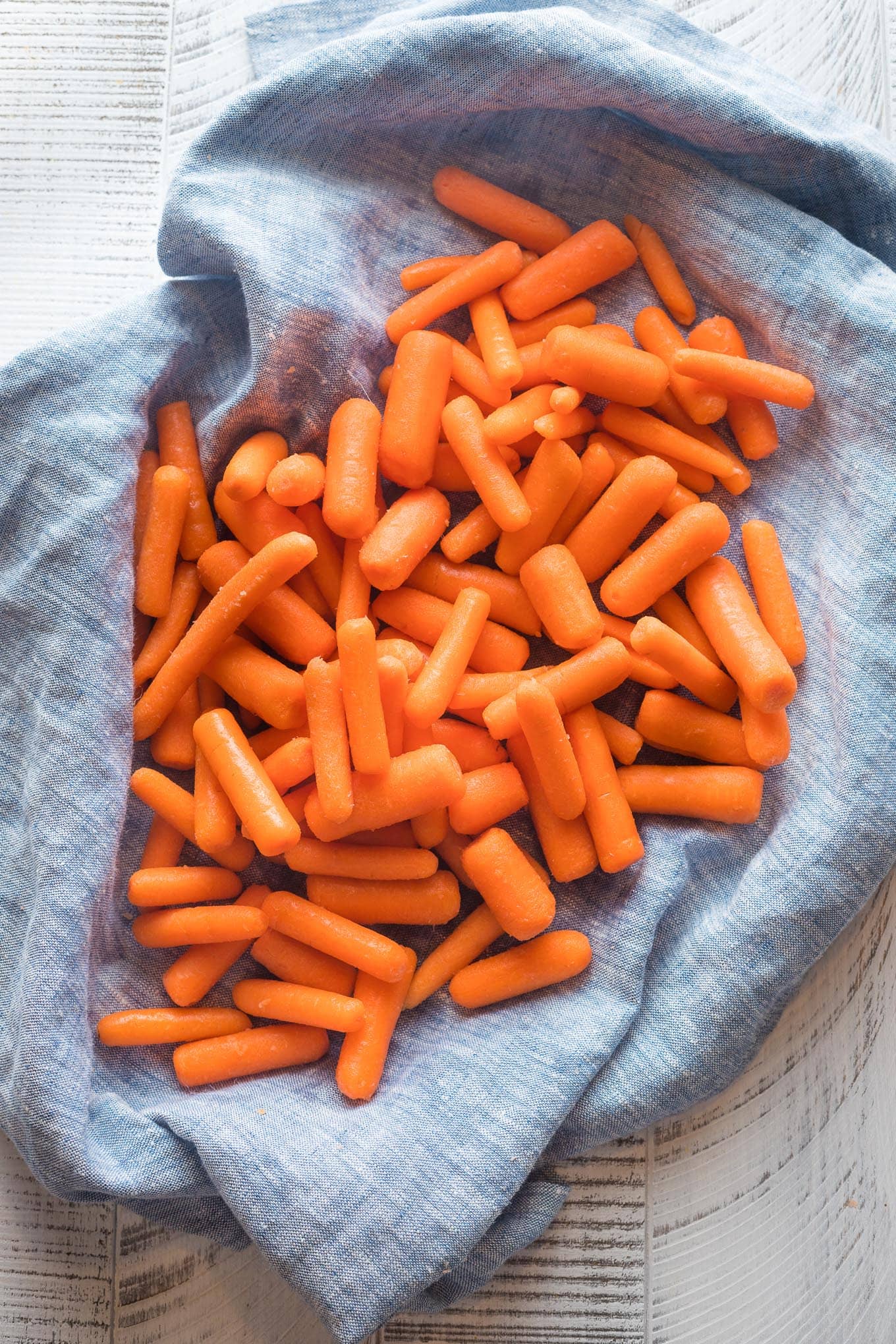 Baby cut carrots being rubbed dry in a blue kitchen towel.