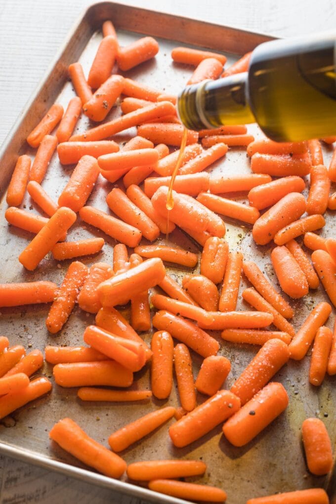 Action shot of olive oil being drizzled over a sheet pan of baby cut carrots.