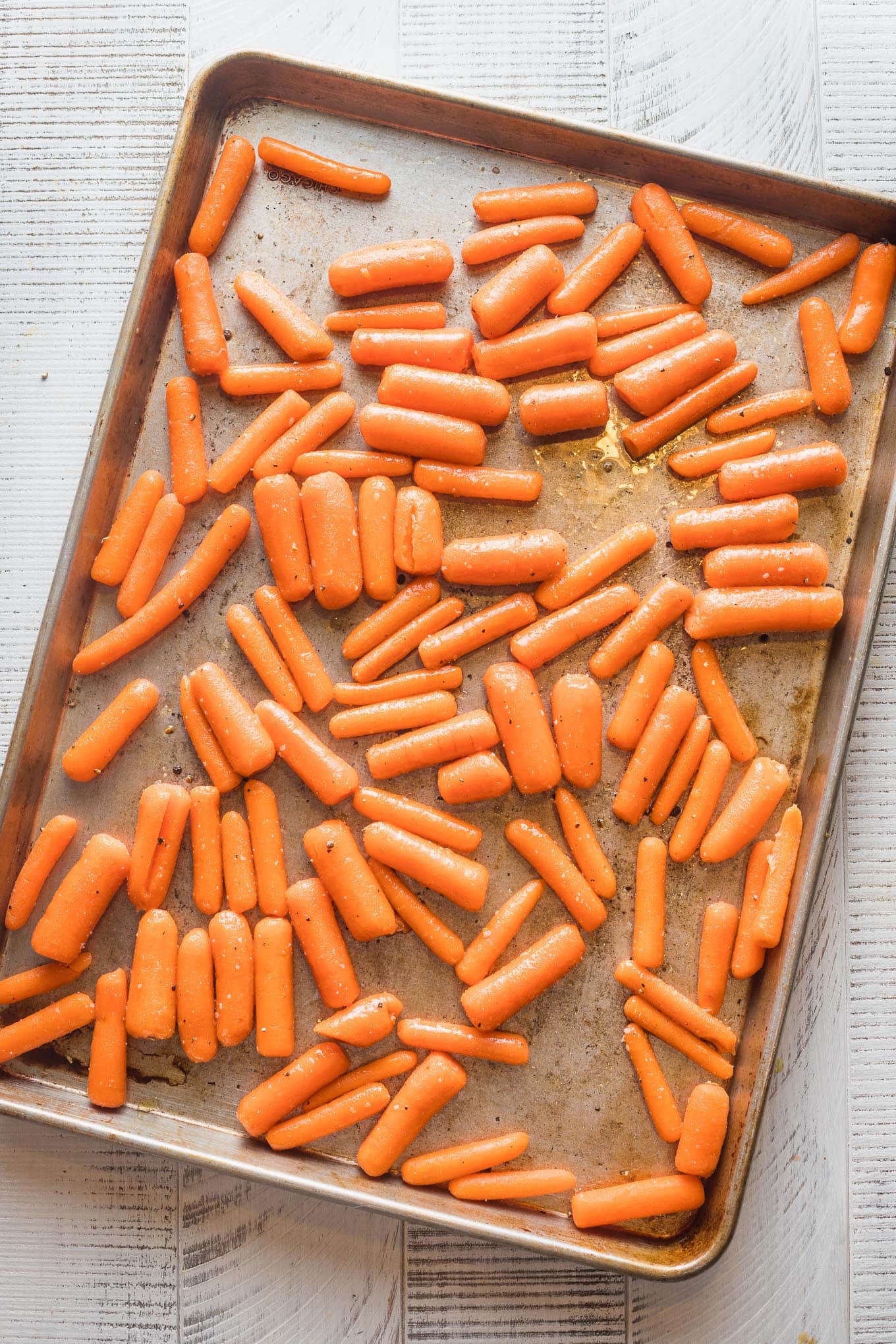 Baby carrots spread in a single layer on a sheet pan, ready to roast.