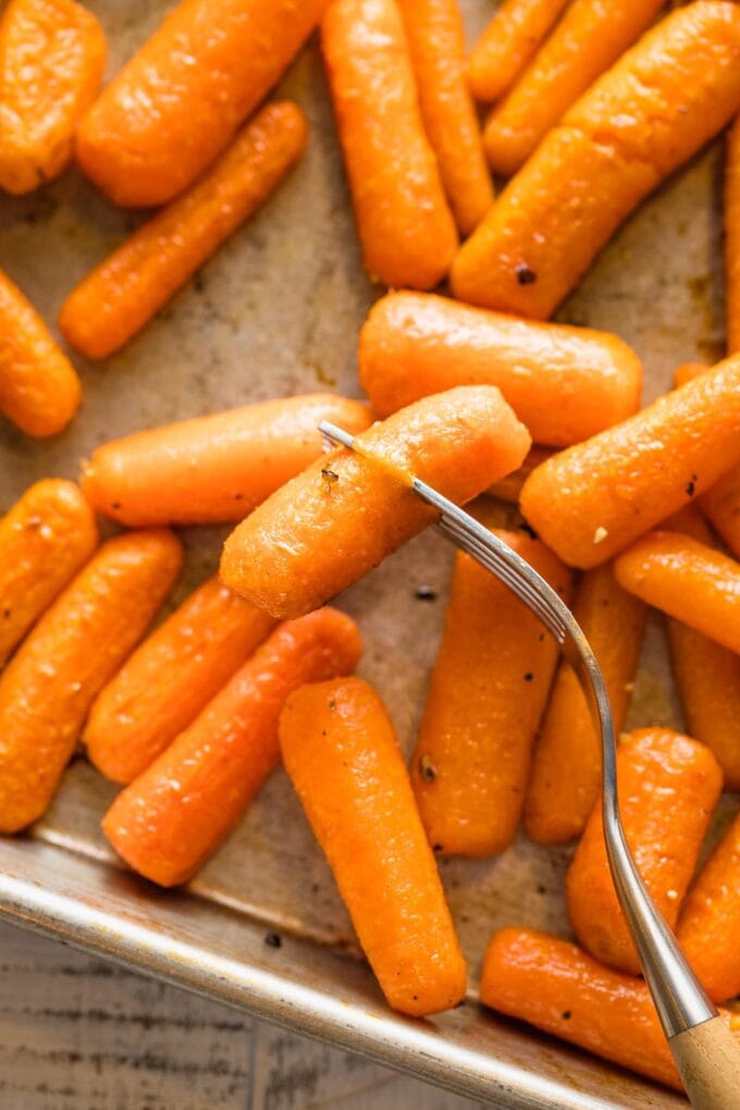 Close up of a fork piercing a tender, slightly wrinkled baby carrot.