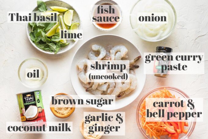 Labeled photo of prep bowls holding raw shrimp, garlic and ginger, carrot and bell pepper, green curry paste, sliced onion, fish sauce, Thai basil, oil, coconut milk, and brown sugar.