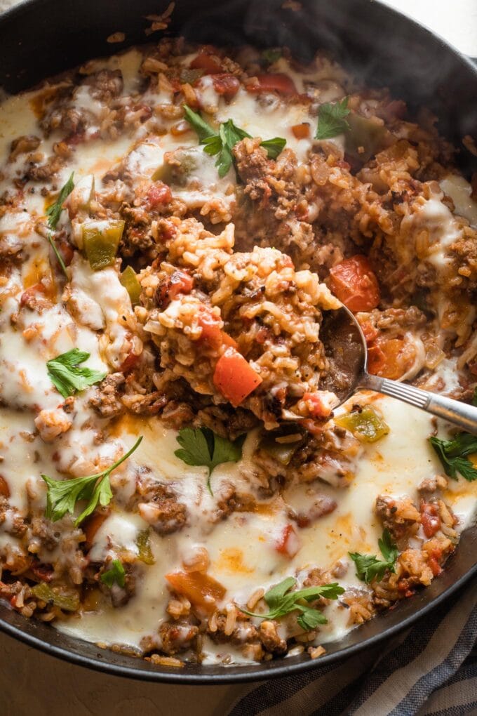 Close up of a spoon scooping up a portion of unstuffed peppers from a skillet to serve.