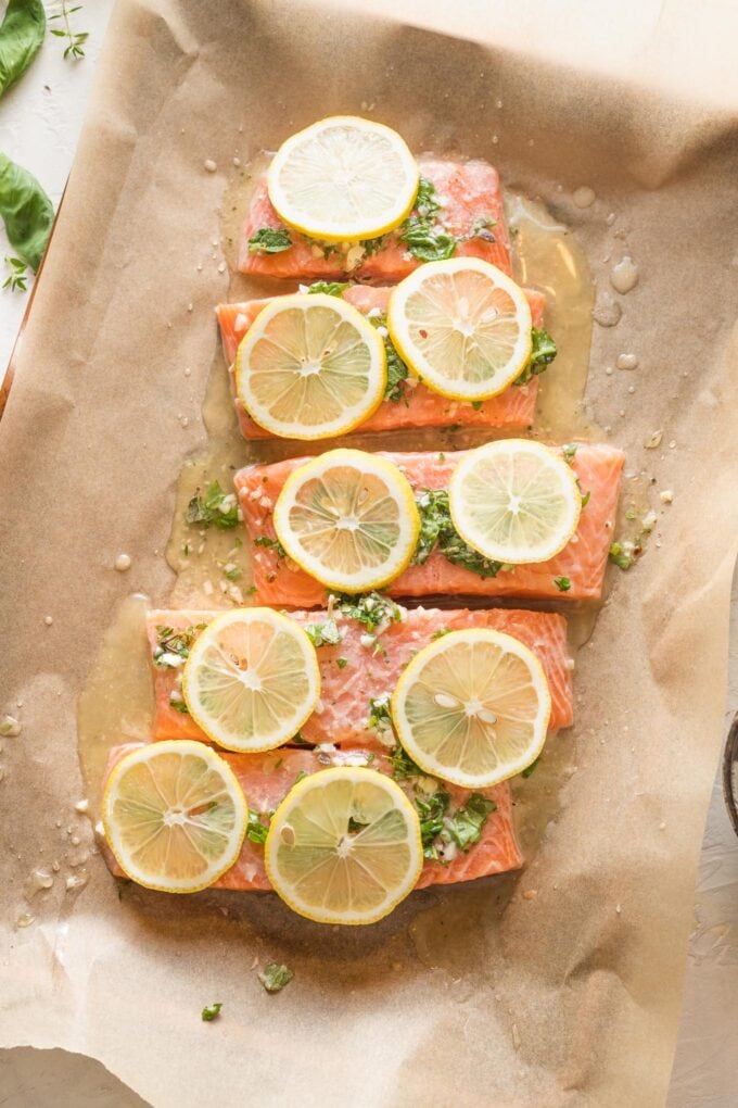 Uncooked salmon with herbs and lemon slices on a baking sheet.