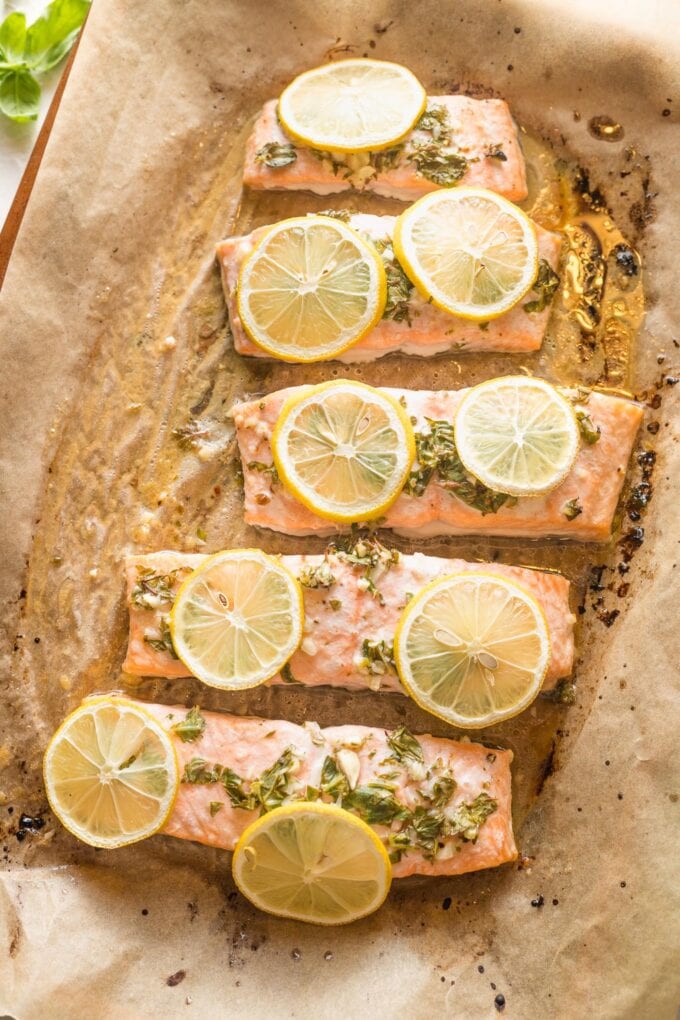 Baked salmon with lemon and herbs on a parchment paper-lined baking sheet.