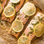 Close up of lemon herb salmon on a parchment lined baking sheet.