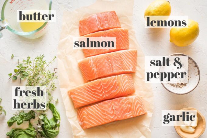 Overhead image of salmon filets, fresh herbs, melted butter, lemons, salt, pepper, and garlic.