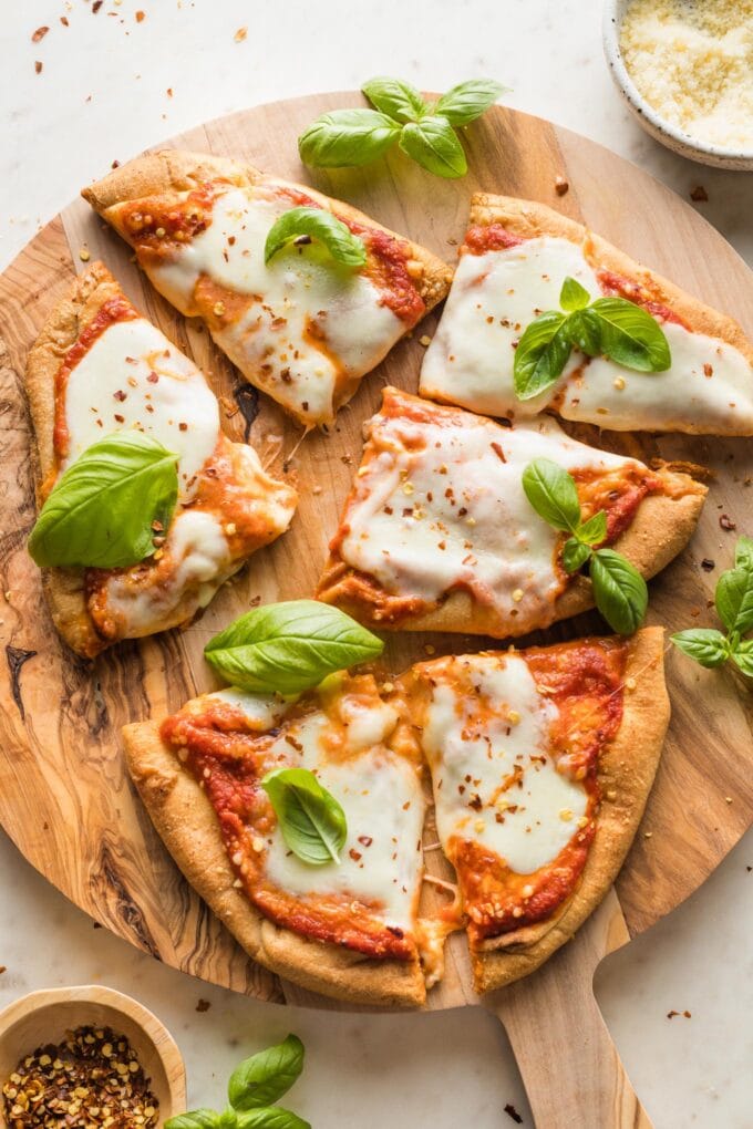 Naan pizza sliced into squares and topped with fresh basil leaves.