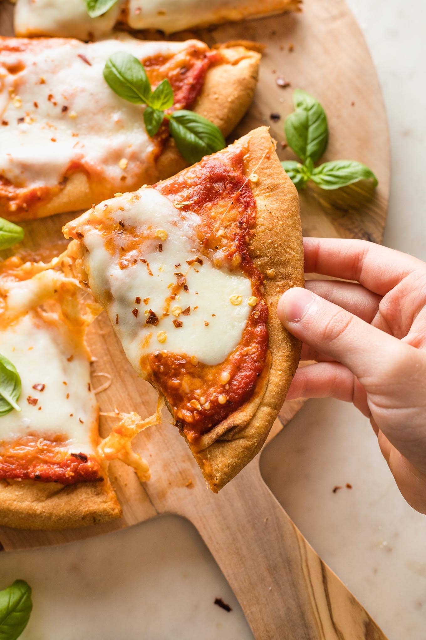 A child's hand grabbing a slice of naan pizza off of a serving board.