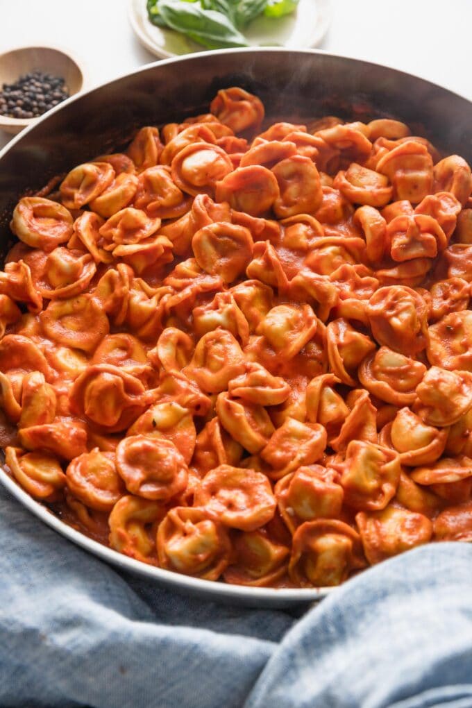 Angled view of creamy tomato tortellini in a low skillet.
