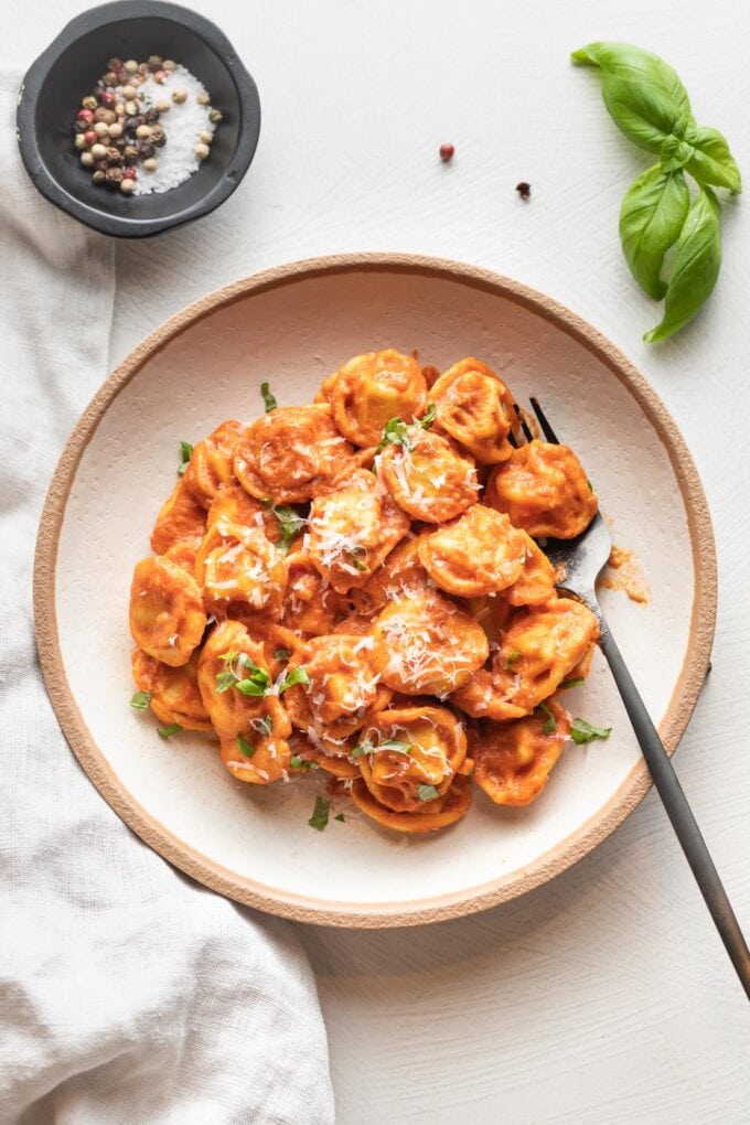 Bowl of tortellini in creamy tomato sauce, garnished with fresh basil and grated Parmesan.
