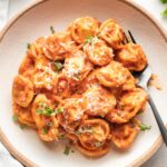 Bowl of tortellini in creamy tomato sauce, garnished with fresh basil and grated Parmesan.