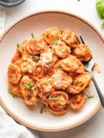 Bowl of tortellini in creamy tomato sauce, garnished with fresh basil and grated Parmesan.