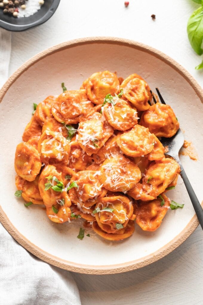 Bowl of tortellini in creamy tomato sauce, garnished with fresh basil and grated Parmesan.