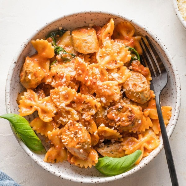 Bowl of Italian chicken sausage pasta garnished with parmesan and basil.