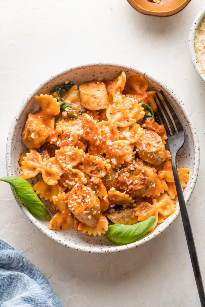 Bowl of Italian chicken sausage pasta garnished with parmesan and basil.