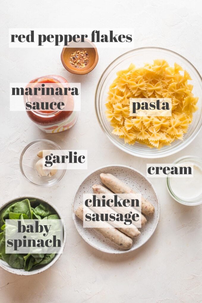 Uncooked pasta, Italian-style chicken sausage links, garlic, baby spinach, cream, marinara sauce, garlic, and red pepper flakes shown in prep bowls.