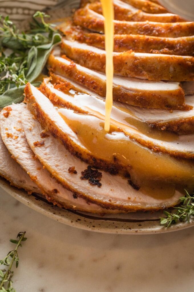 Close-up of gravy being poured over turkey breast.