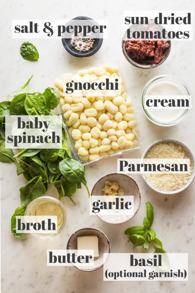 Labeled photo showing shelf-stable gnocchi, baby spinach, cream, broth, sun-dried tomatoes, garlic, butter, Parmesan, basil, salt, and pepper, all laid out in prep bowls ready to cook.