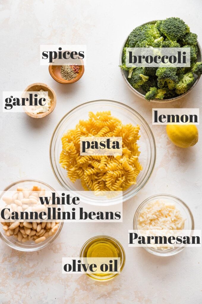 Labeled photo of prep bowls containing dried pasta, broccoli florets, white Cannellini beans, olive oil, Parmesan, lemon, garlic, and dried spices.