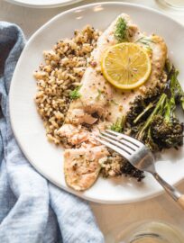 Close up of baked rainbow trout served on a plate, being flaked with a table fork.