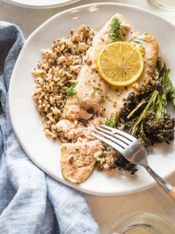 Close up of baked rainbow trout served on a plate, being flaked with a table fork.