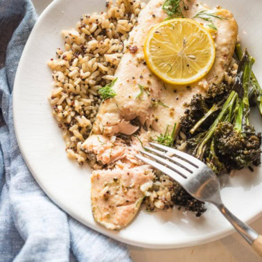 Close up of baked rainbow trout served on a plate, being flaked with a table fork.