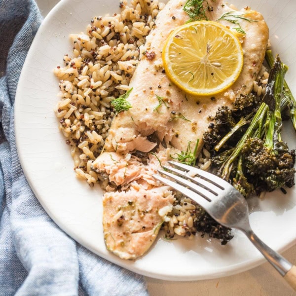 Close up of baked rainbow trout served on a plate, being flaked with a table fork.