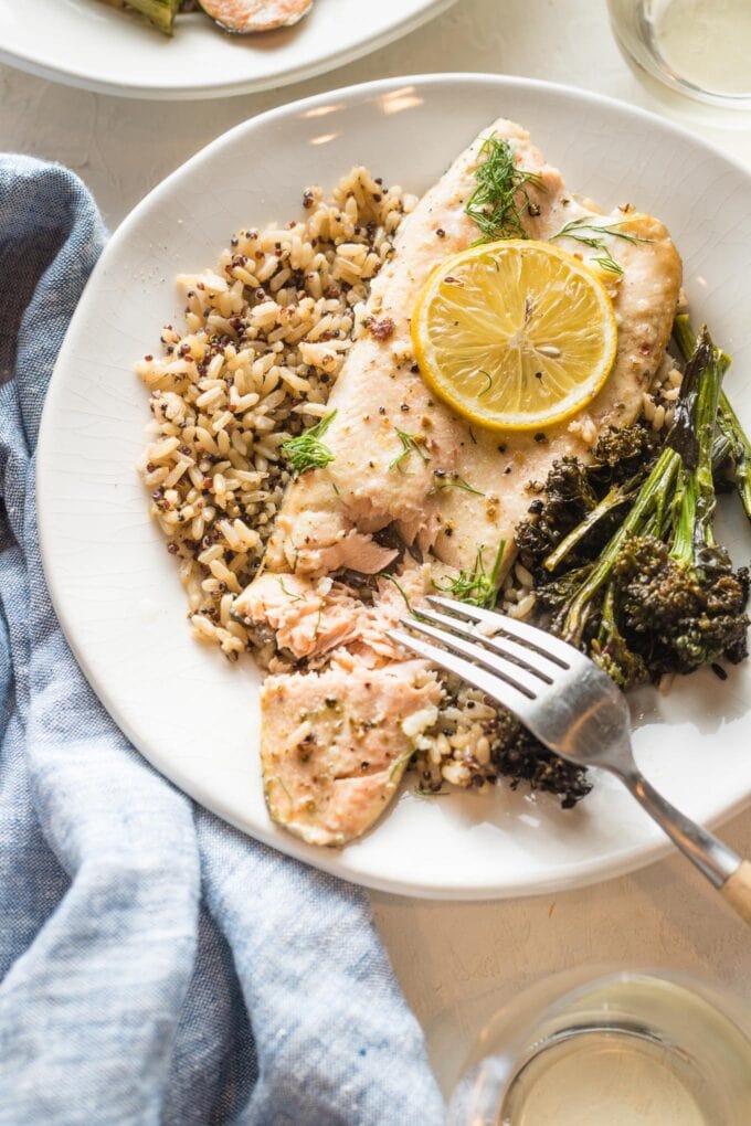 Close up of baked rainbow trout served on a plate, being flaked with a table fork.