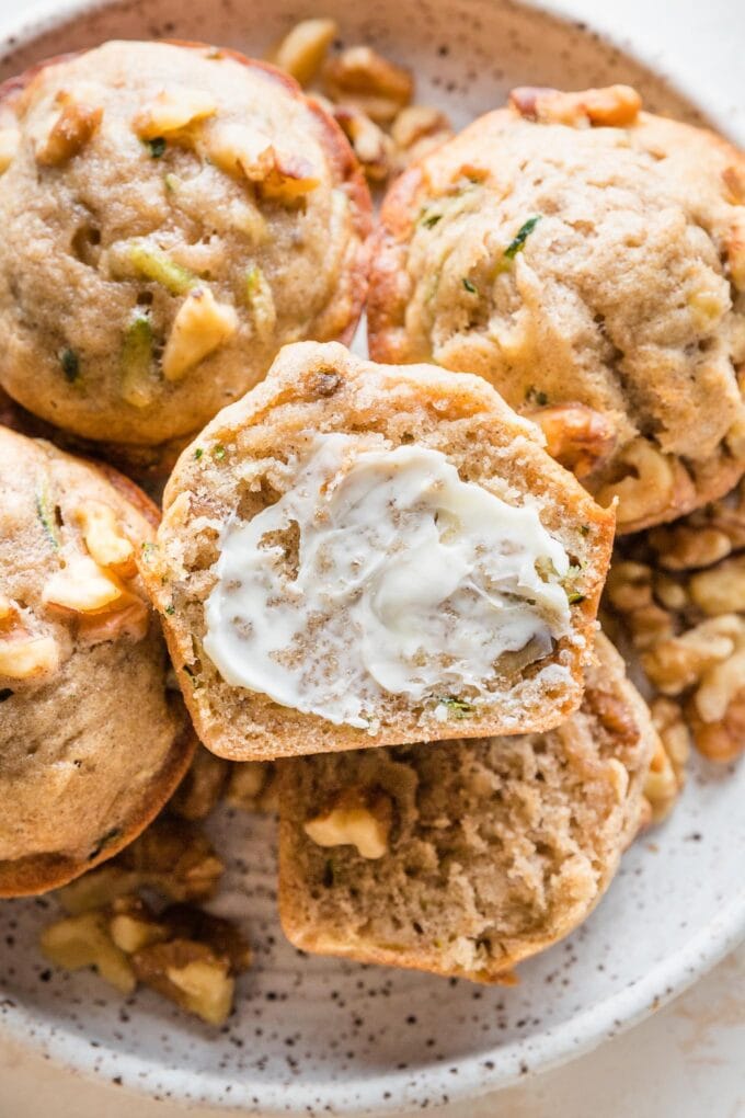 Close up of a banana zucchini muffin cut open and slathered with softened butter.