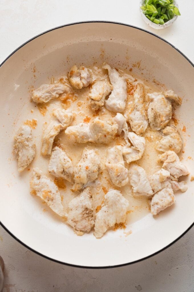 Browned pieces of chicken breast in a large skillet.