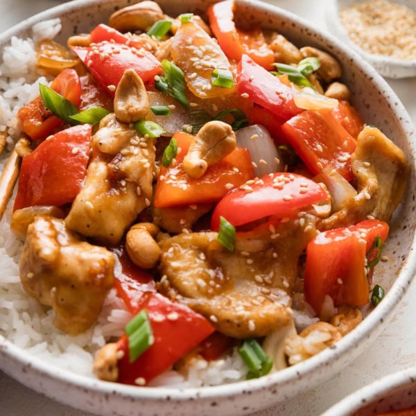 Angled view of a low bowl filled with a stir fry with thin sliced chicken, onions, bell peppers, and cashews.