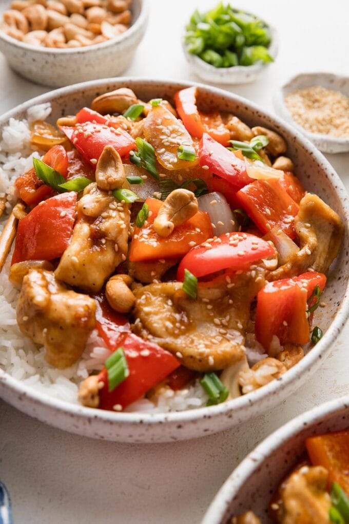 Angled view of a low bowl filled with a stir fry with thin sliced chicken, onions, bell peppers, and cashews.