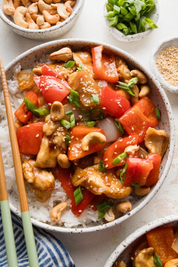 Bowl of chicken and bell pepper stir fry with onions served with cashews, green onions, and white rice.